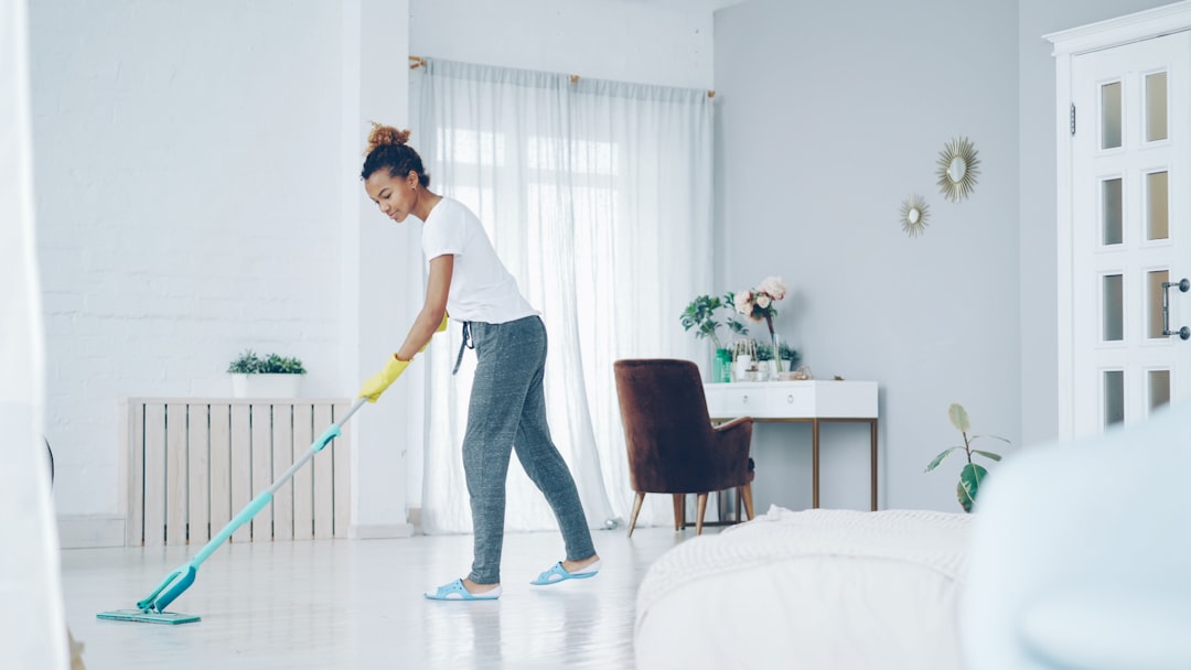 brand-02 Pretty African American girl is mopping the floor at home with a flat plastic mop, wearing gloves and comfortable home clothes. Modern interiors, cleanliness, and a young people concept.